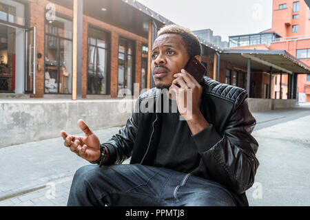 Dark-skinned unpleasantly surprised and annoyed man talking by mobile phone. Stock Photo
