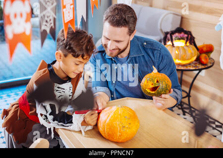 Boy wearing skeleton costume holding red marker coloring pumpkin for Halloween Stock Photo