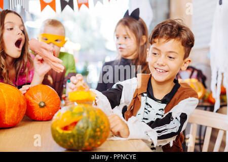 Dark-haired boy wearing skeleton costume for Halloween opening little pumpkin Stock Photo