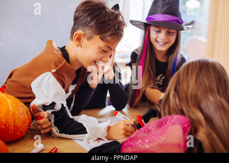 Boy wearing skeleton Halloween costume helping his sister coloring picture Stock Photo