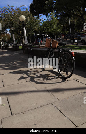 A black ladies bicycle is secured to a bike stand on the wide pavement of Lord Street in Southport, the strong autumn sunshine creates long shadows. Stock Photo