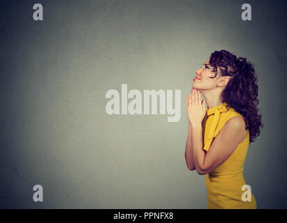 Side view of helpless woman holding hands together with feeling of apology and making request on gray background Stock Photo