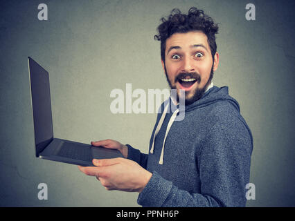 Surprised young man with laptop computer looking at camera in astonishment Stock Photo