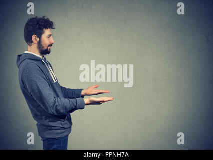 Side view of man with hands extended looking away while asking for help on gray background Stock Photo