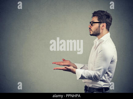 Side view of man with hands extended looking away while asking for help on gray background Stock Photo