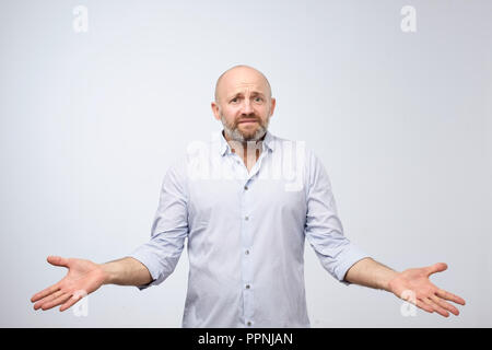 Confused mature bearded man standing and shrugging shoulders isolated over white background. Stock Photo