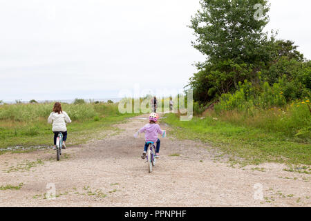 Family riding bikes together on Mackinac Island, Michigan. Bike path along coast of Lake Huron, one of the Great Lakes. Stock Photo