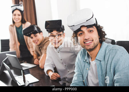 group of multiethnic business partners with virtual reality headsets at table with laptops in modern office Stock Photo