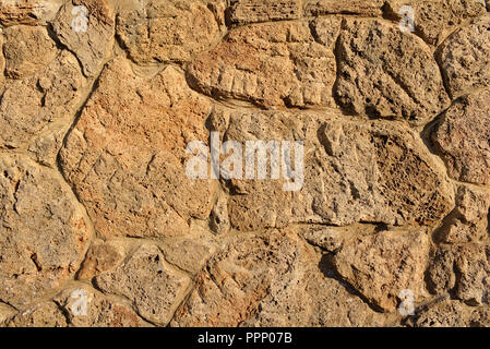 Sandstone wall made of irregular porous pieces of stone lit by the evening sun Stock Photo