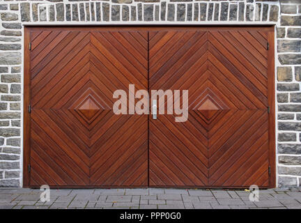 Old gray stone wall with double-leaved wooden herringbone garage door Stock Photo