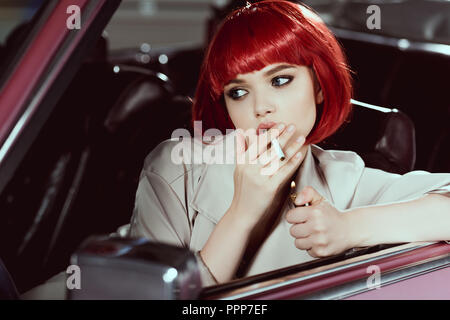 attractive girl in red wig smoking cigarette and looking away while