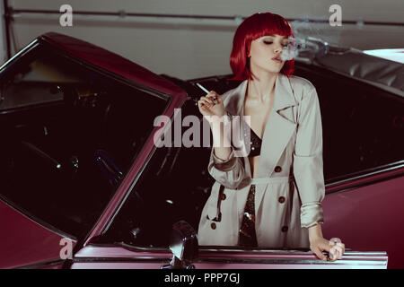 stylish girl in bra and trench coat standing near retro car Stock