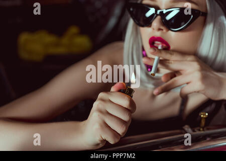 close-up view of stylish blonde girl in beret and sunglasses smoking cigarette in car Stock Photo