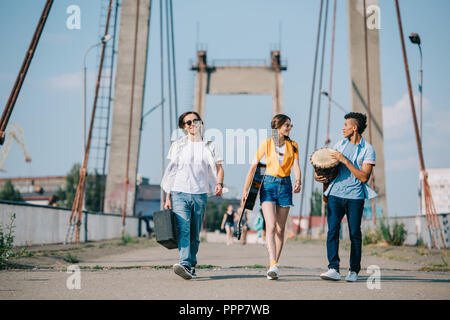 Young male and female buskers carrying instruments on sunny city street Stock Photo