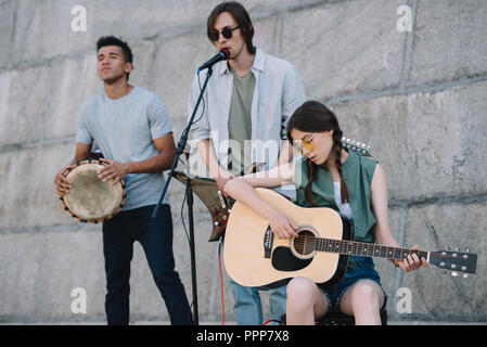 Young and happy male and female street musicians playing guitars and djembe in city Stock Photo