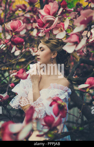 Young caucasian girl among pink magnolia flowers. Stock Photo