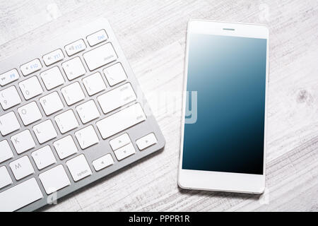 Smartphone With Reflection Lying Next To A White Keyboard On A Table Stock Photo