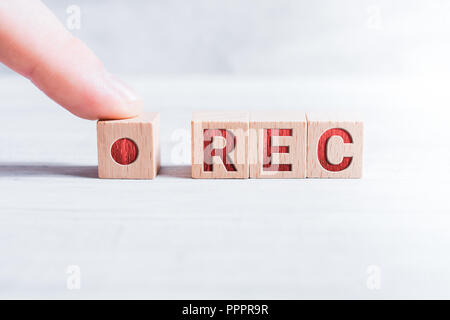 The Abbreviation REC Formed By Wooden Blocks And Arranged By A Male Finger On A White Table Stock Photo