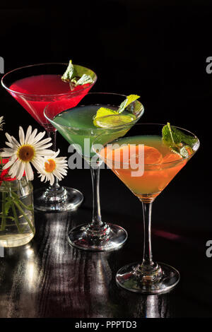 Kiwi, orange and cherry jelly with lime pieces in the glasses topped mint leaves and flowers on the black background Stock Photo