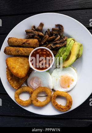 Close up of a vegetarian english breakfast containing beans in tomato sauce, fried eggs, onion rings, oven baked vegetables, mushrooms and avocado. Stock Photo