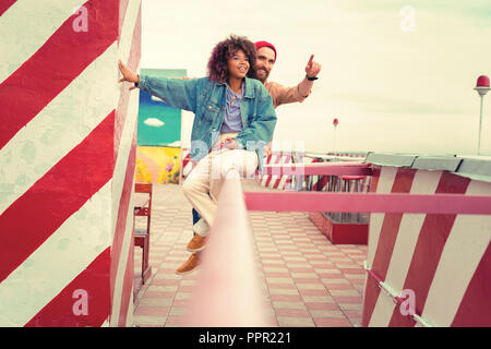 Two loving people wearing casual clothes and sitting on the hand rail Stock Photo