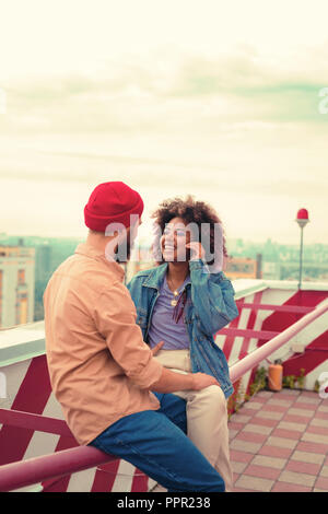 Young woman smiling happily while sitting on the roof with her beloved man Stock Photo