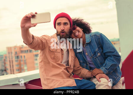 Playful young couple making silly faces while taking selfies Stock Photo