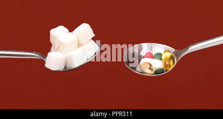 Silver spoons full with white sugar cubes and colorful pills both considered as unhealthy Stock Photo