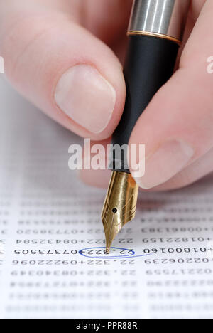 Woman's hand holding pen, stock quotes in background Stock Photo