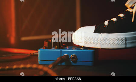 Close up of guitar player foot pressing pedal. Musician uses music effect loop machine. Man in trendy sneakers, his foot playing at stage during concert. Macro view Stock Photo