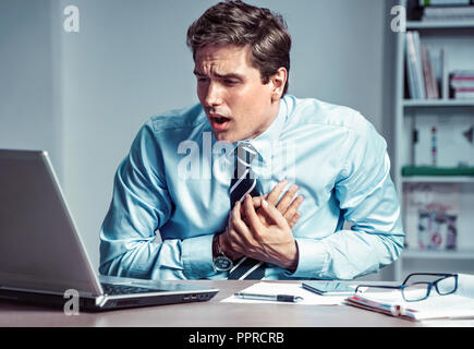 Office manager having heart attack. Photo of young man holding hand on painful chest in the workplace. Medical concept. Stock Photo