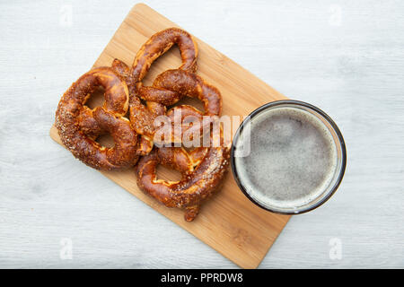 Freshly baked homemade soft pretzel with salt on wooden cutting board with glass of beer. Stock Photo