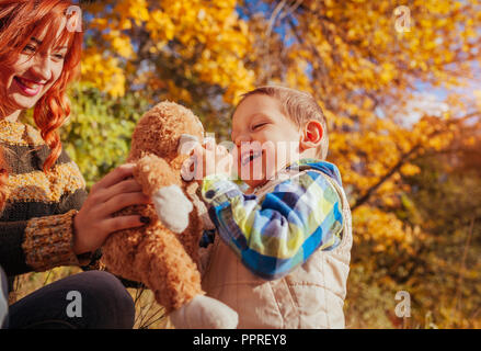Happy mother and her little son walking and having fun in autumn forest. Kid is playing with a toy Stock Photo
