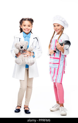 schoolchildren in costumes of doctor and chef standing with teddy bear and frying pan isolated on white Stock Photo