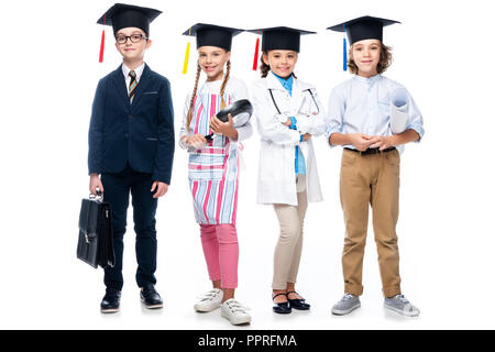 schoolchildren in costumes of different professions and graduation caps looking at camera isolated on white Stock Photo