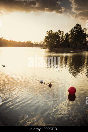 Red buoy in the golden waters by the sunset sun with the sky with clouds in the background Stock Photo