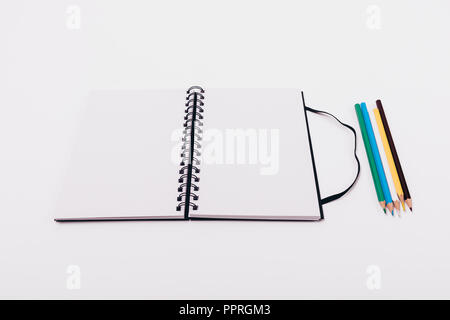 Mock-up open notepad with spring with two blank sheets on white table near colored pencils. Stock Photo