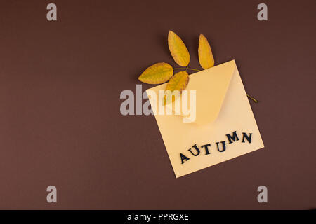 Yellow autumn leaves and envelope for writing on a brown background. Top view. Free space for text. Postcard in the style of minimalism. Copy space Stock Photo