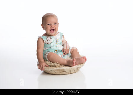 A laughing seven month old baby boy sitting in a rustic, wooden bowl. Shot in the studio on a white, seamless backdrop. Stock Photo