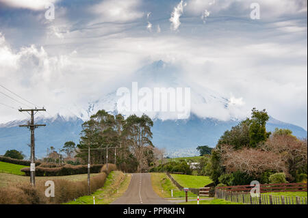 Mount Taranaki (Mount Egmont), Egmont National Park, New Zealand. Rural landscape, road leads to mountain semi-covered in cloud with green foreground. Stock Photo