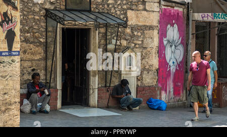 Athens Greece/August 17, 2018: Two homeless men sitting in front of chruch with people walking by Stock Photo