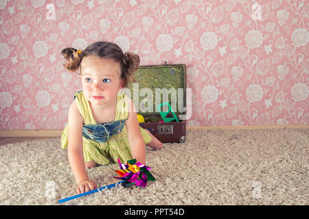 little girl smiling, sitting on the floor in the studio, behind her suitcase with toys. Stock Photo