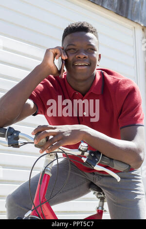 Teenage Boy On Bike Talking on Mobile Phone Outdoors Stock Photo