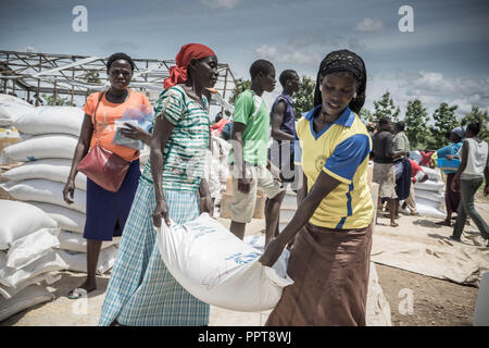 Female South Sudanese refugees seen carrying a bag of 50KG food supply from the distribution point at Bidi Bidi refugee settlement. Stock Photo