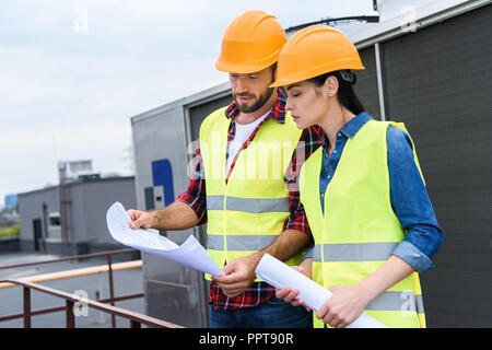 professional architects in helmets working with blueprints on roof Stock Photo