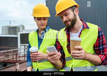engineers in helmets using smartphone on coffee break on roof Stock Photo