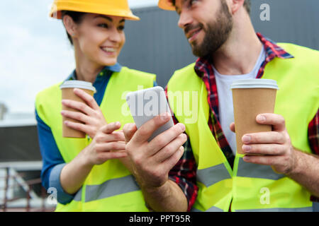 architects in safety vests and helmets using smartphone on coffee break Stock Photo
