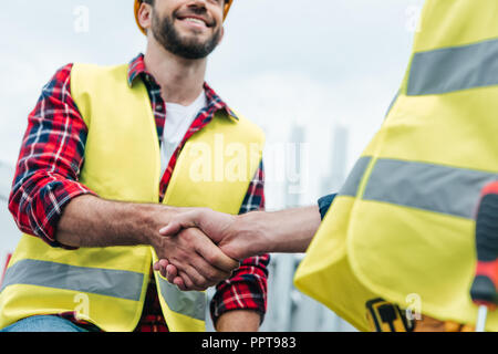 cropped view of engineers in safety vests shaking hands on roof Stock Photo