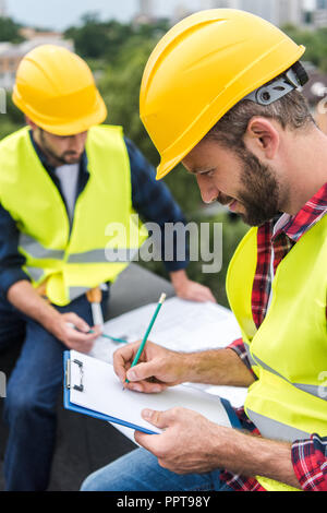 architects in safety vests and hardhats, one of them writing on clipboard Stock Photo