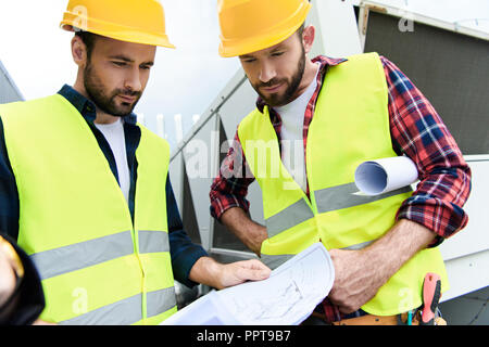 two architects in safety vests and helmets looking at blueprints Stock Photo
